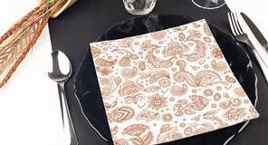 Cubierto con plato negro, servilleta estampada, cubiertos y follaje decorativo.