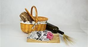 Cesta de picnic con pan, una botella de vino y comida envuelta sobre una tabla de madera.
