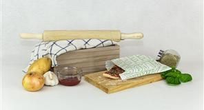 Rodillo y alimentos sobre una superficie blanca: patatas, cebollas, albahaca, mermelada, hierbas y una porción de pizza en una bolsa.