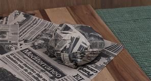 Pelota envuelta en papel de periódico sobre una superficie de madera, al lado de una alfombra verde.