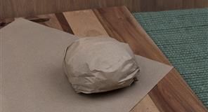 Artículo envuelto en papel marrón sobre una tabla de cortar, con una hoja de papel marrón debajo.