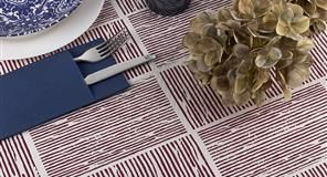 Mesa preparada con plato azul, cubiertos en funda azul y flores secas sobre un mantel estampado.