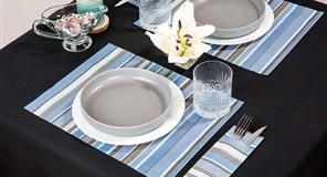 Mesa con platos grises, manteles individuales a rayas azules y un lirio sobre un mantel negro.