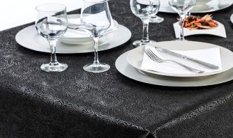 Puesta de mesa con vasos, platos, cubiertos y comida sobre un mantel oscuro.