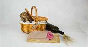 Cesta de picnic con pan, botella de vino y carne sobre tabla de madera.