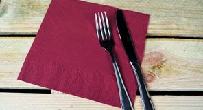 Tenedor y cuchillo sobre una servilleta de color burdeos, colocada sobre una superficie de madera clara.