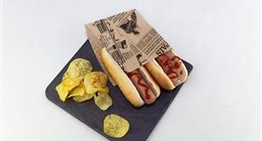 Perros calientes con ketchup en bolsa de periódico, patatas fritas en pizarra.