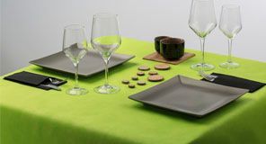 Mesa con platos cuadrados grises, cristalería y mantel verde.