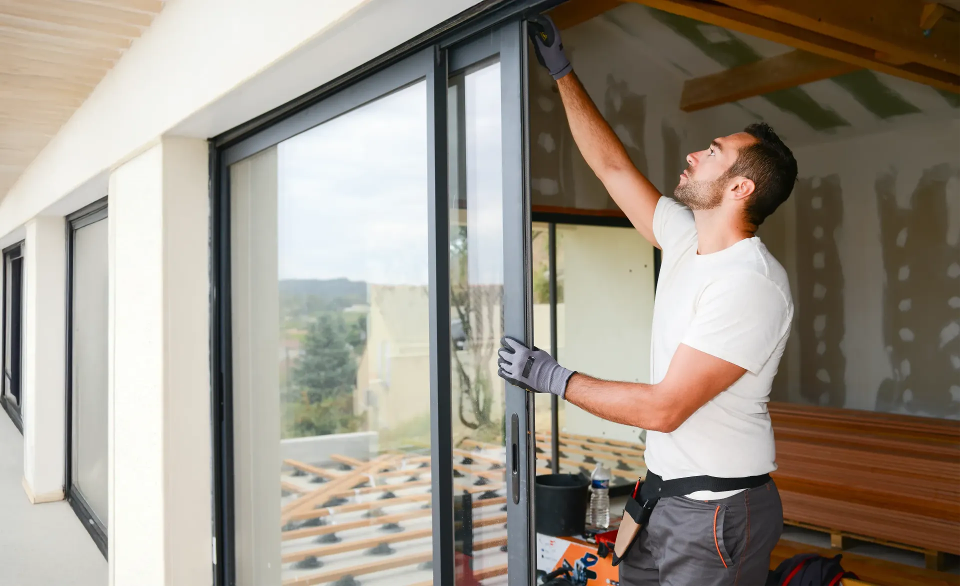 Persona con guantes instalando una puerta corrediza de vidrio en el interior de un edificio en construcción.