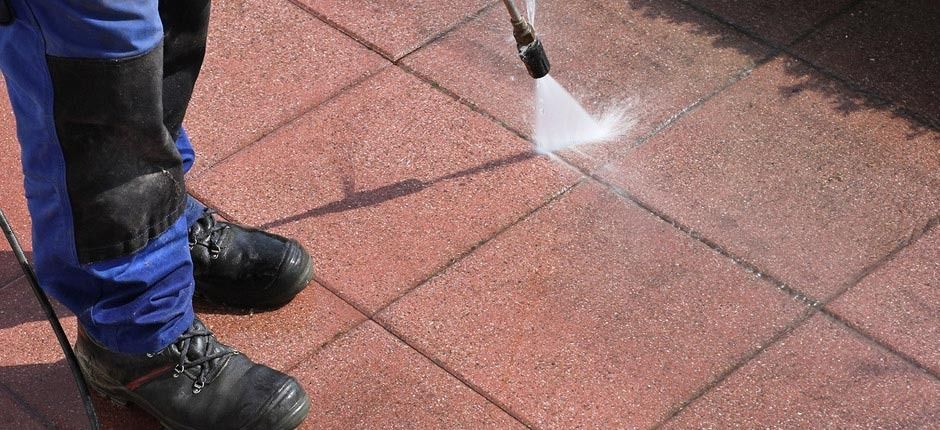 Una persona está usando una hidrolavadora para limpiar una pasarela de ladrillos.