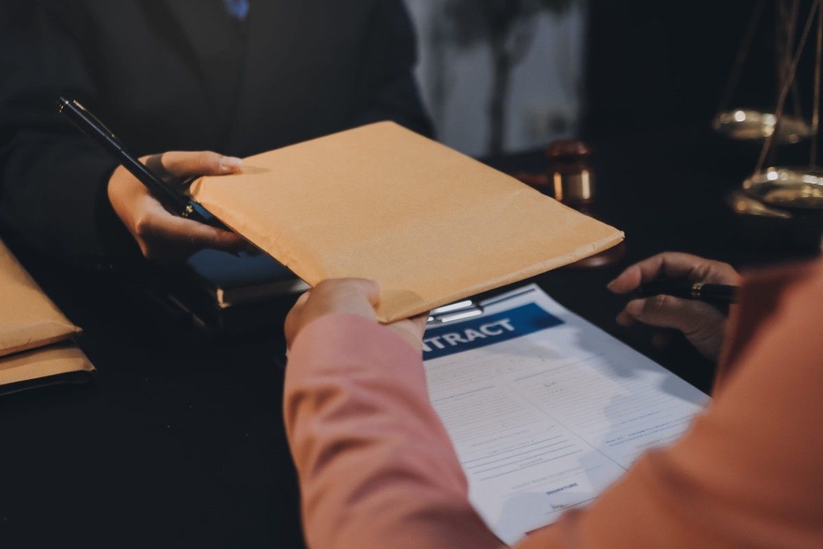 Dos personas vestidas de etiqueta intercambian un sobre de papel manila sobre un documento etiquetado como 