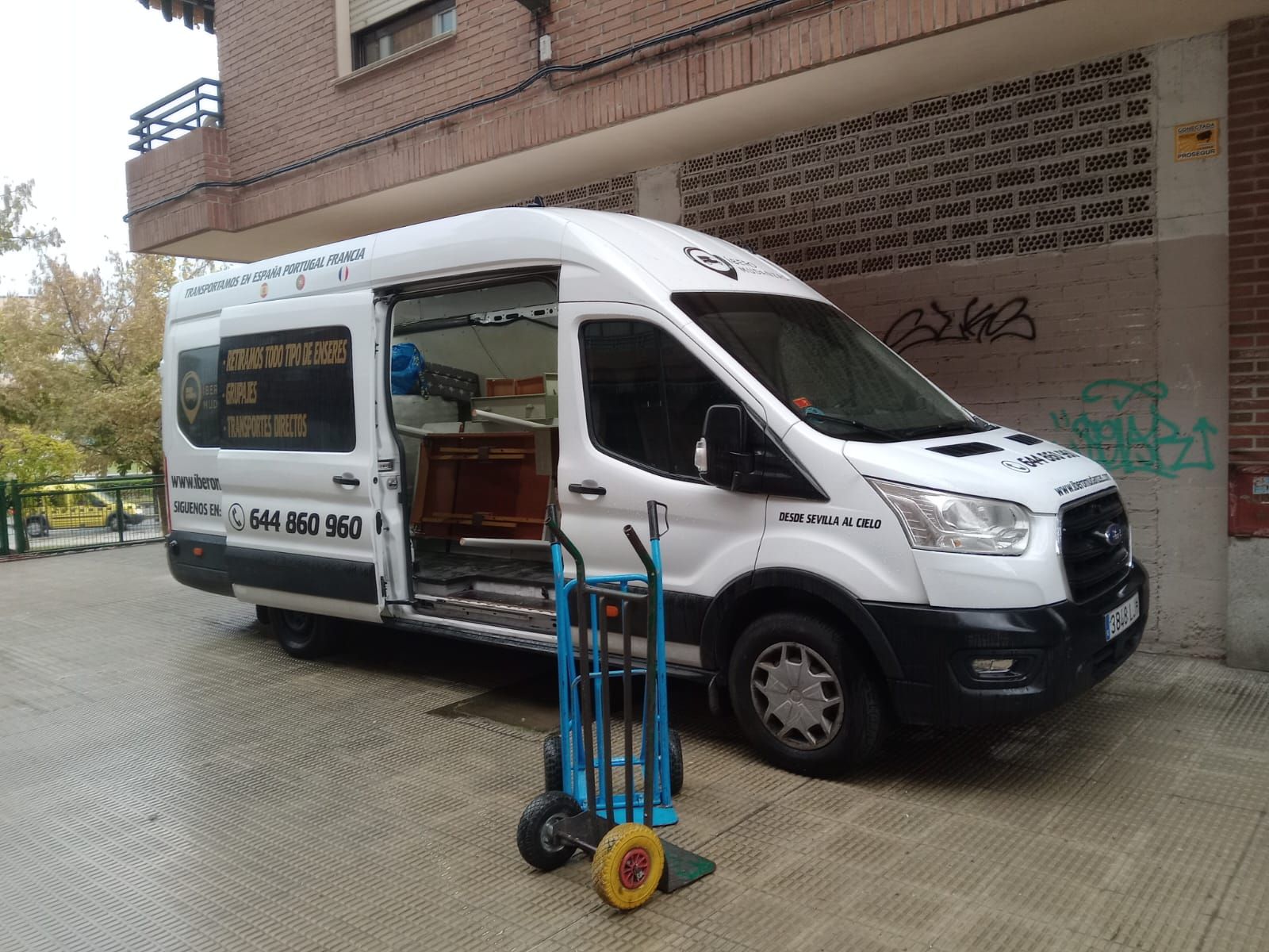 Una camioneta blanca está estacionada frente a un edificio con la puerta abierta.