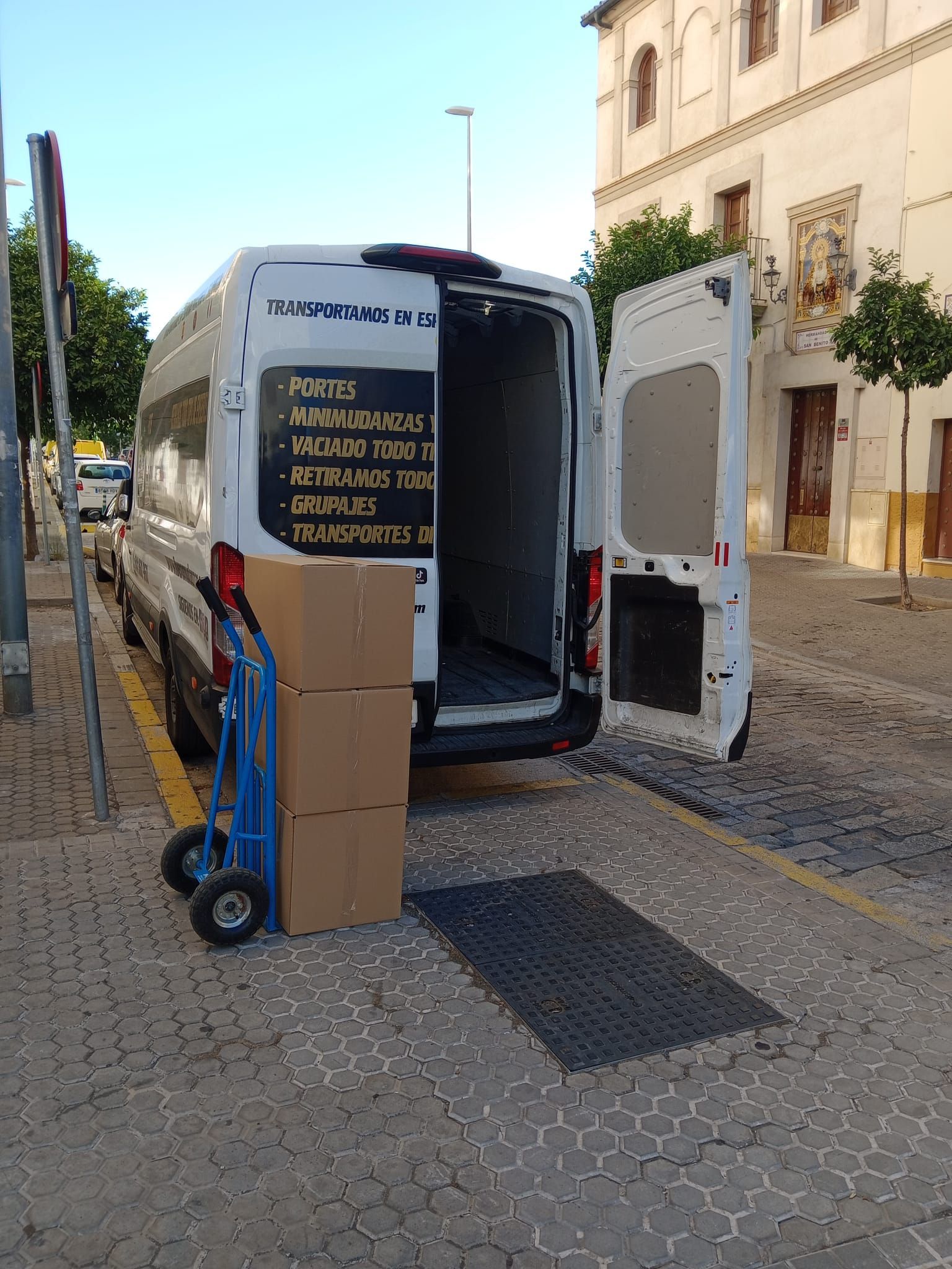 Una camioneta blanca está estacionada al costado de la carretera con la puerta abierta y cajas en la parte trasera.