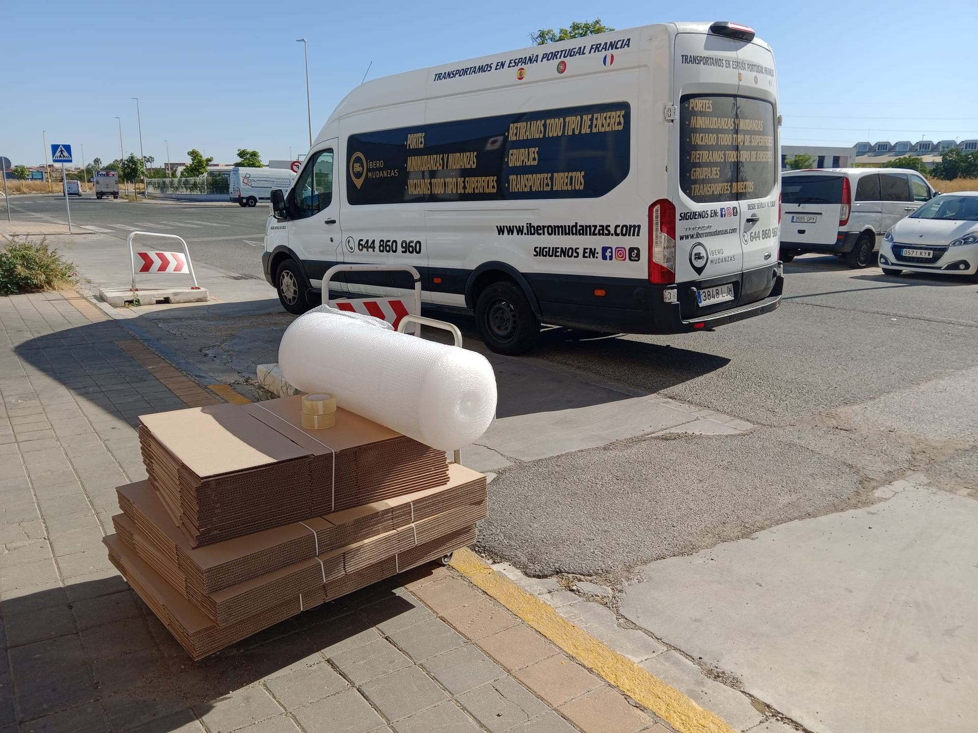 Una furgoneta blanca está aparcada junto a una pila de cajas de cartón.