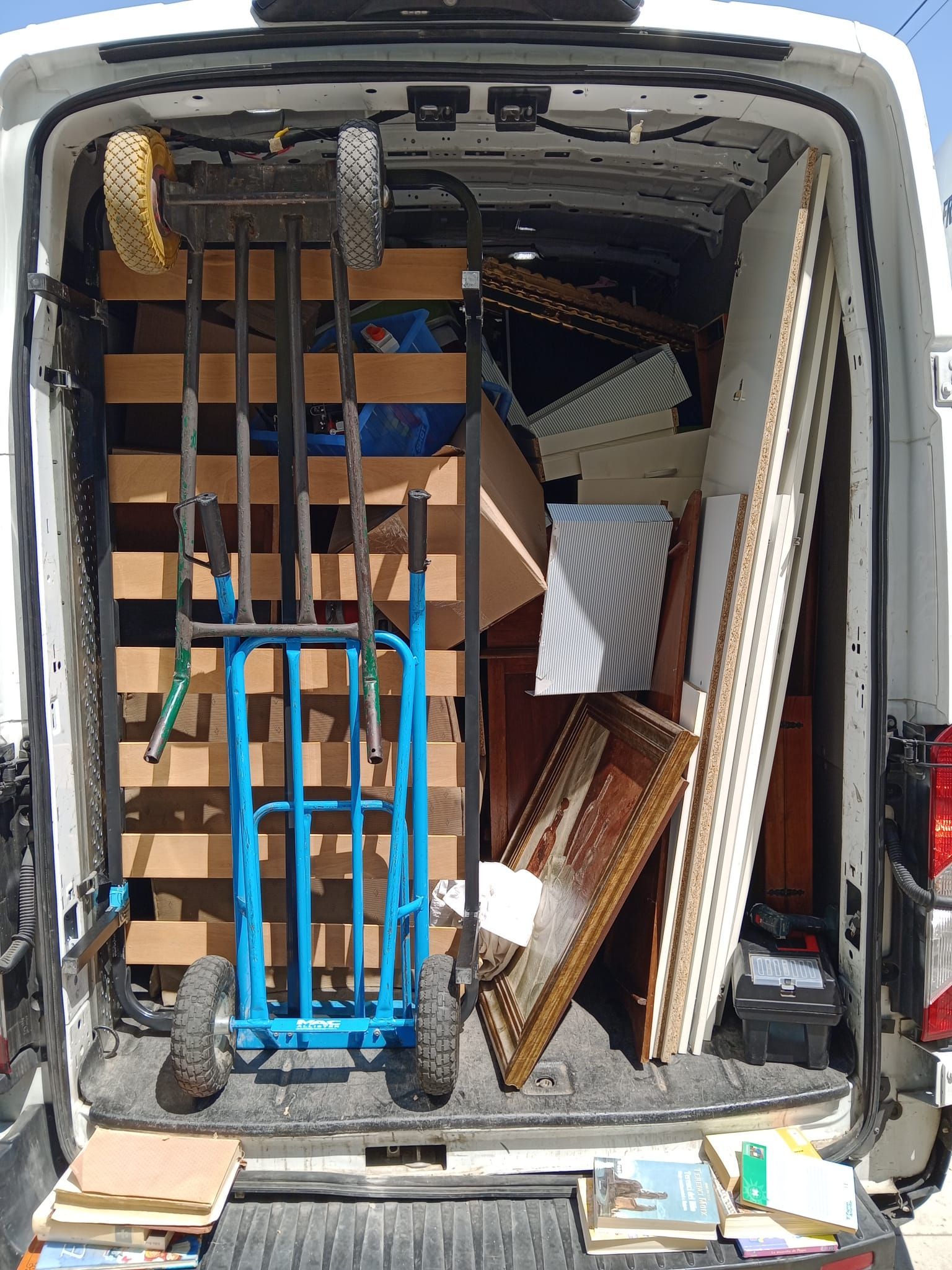 La parte trasera de una camioneta blanca está llena de muebles y una carretilla de mano.
