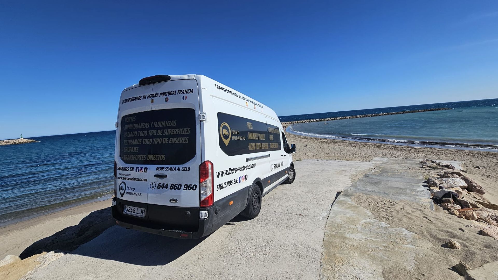 Una camioneta blanca está estacionada en la playa junto al océano.