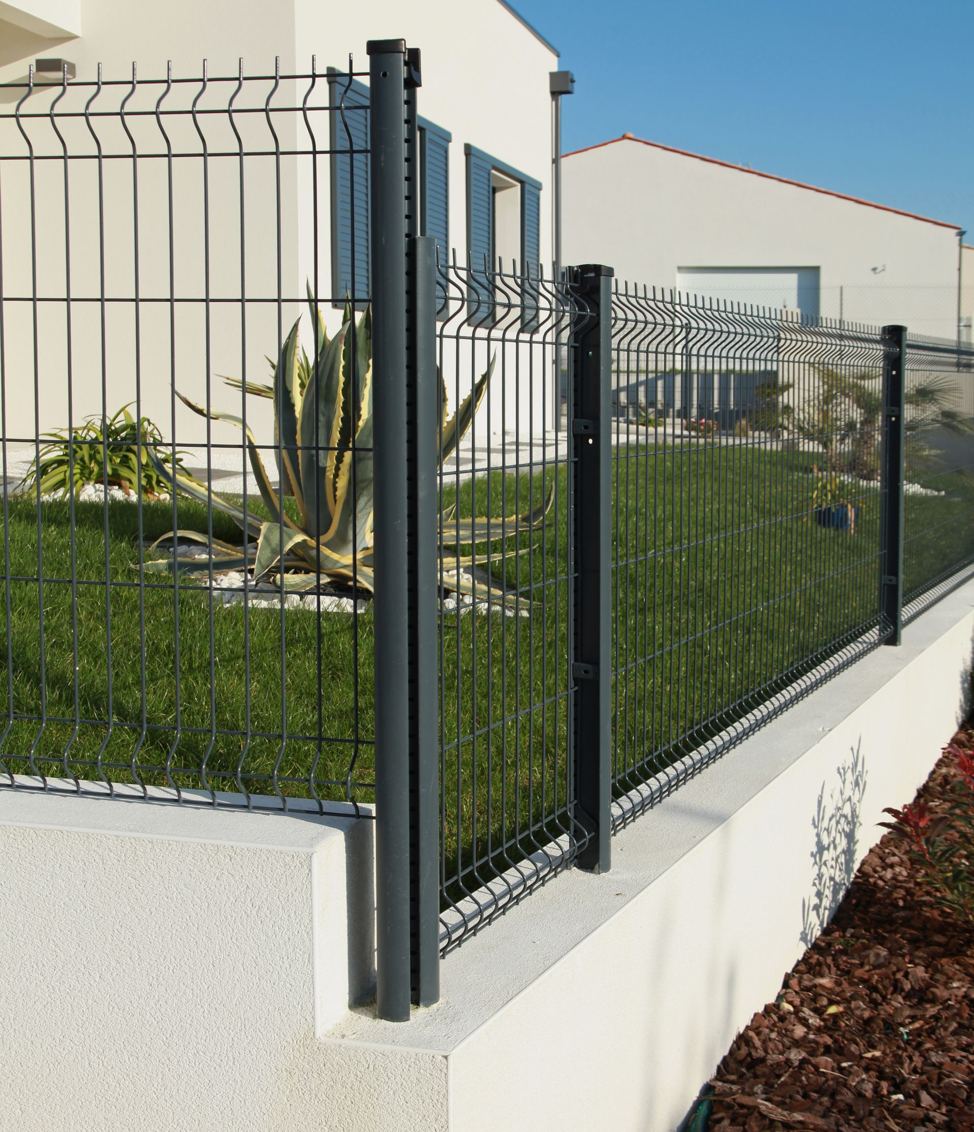Un muret sous le grillage rigide sécurisant une maison.