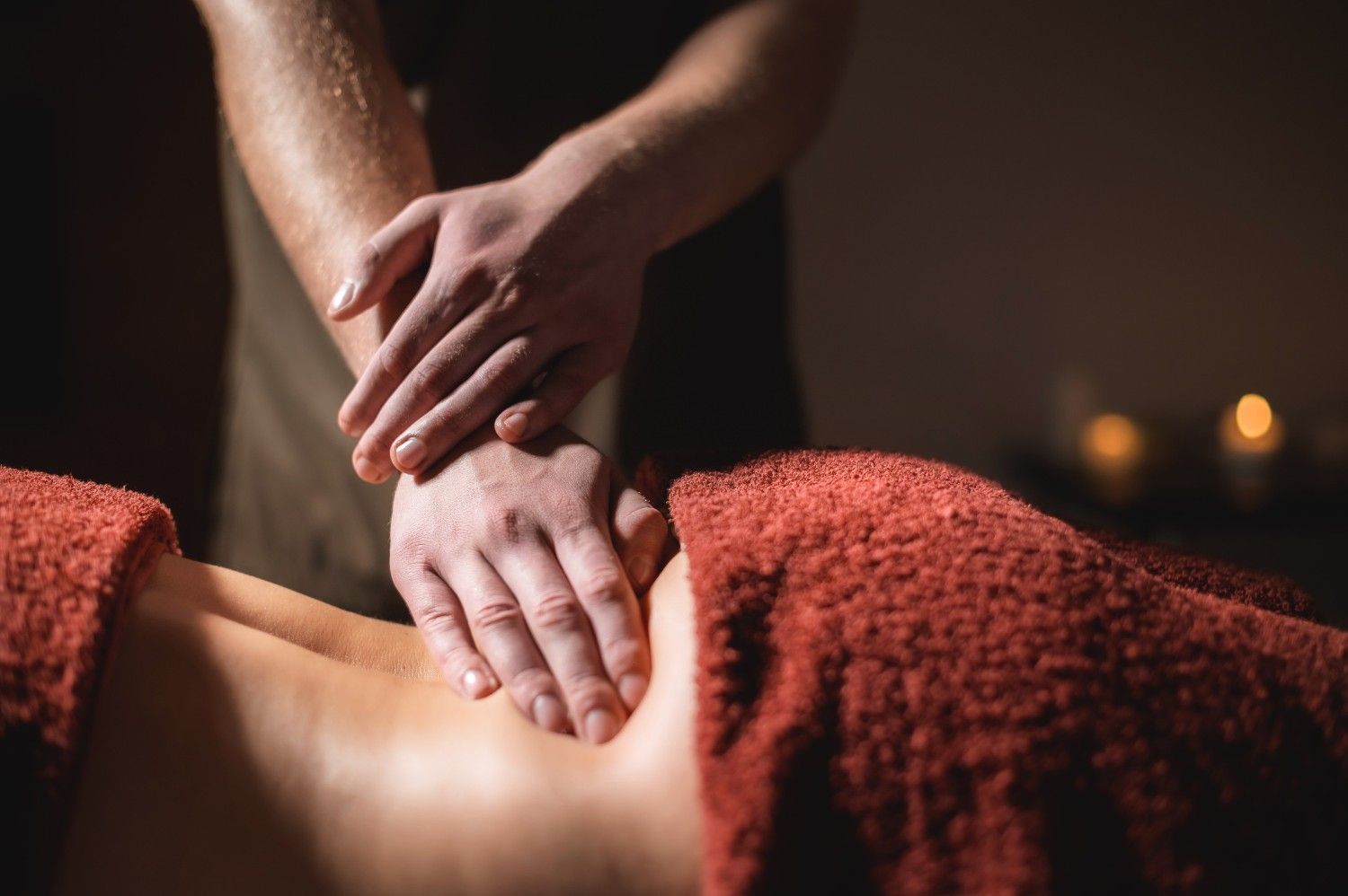 Manos masajeando el abdomen de una persona, cubiertas con una toalla roja. Iluminación tenue.