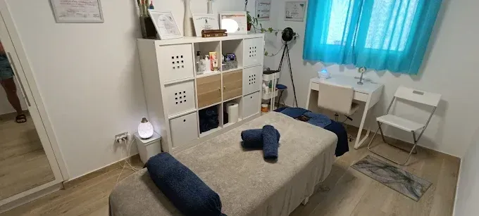 Una sala de terapia de masajes con mesa de masajes, estantes de almacenamiento, escritorio y silla.