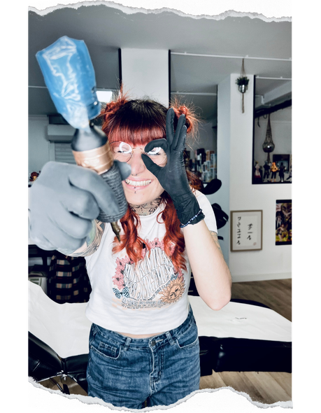 Une femme tient une machine à tatouer devant son visage.