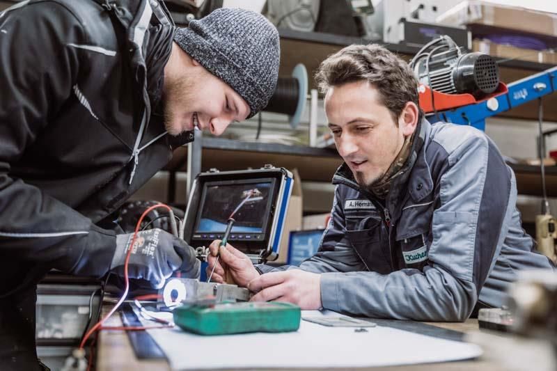 Zwei Männer arbeiten in einer Garage an einem Gerät.