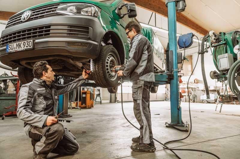 Zwei Männer arbeiten in einer Garage an einem grünen Lieferwagen.