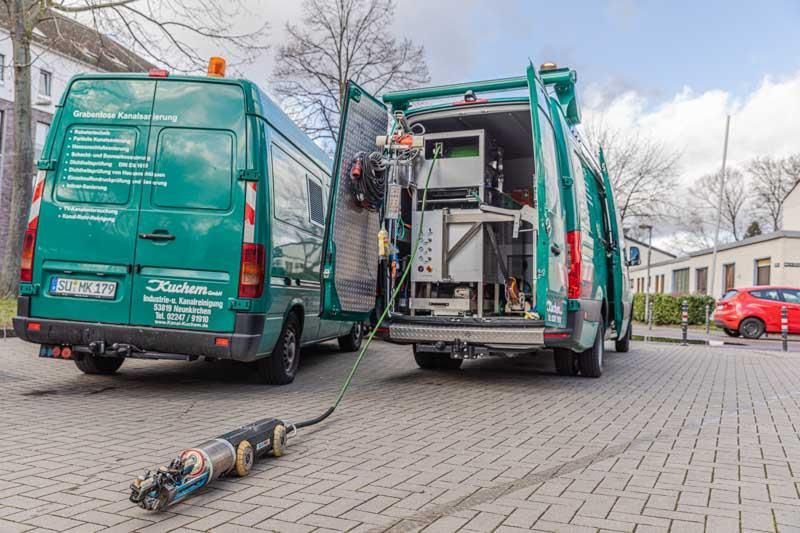 Zwei grüne Lieferwagen parken nebeneinander auf einem gepflasterten Gehweg.