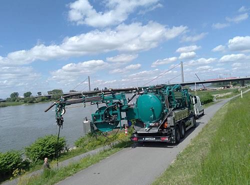 Ein grüner Lastwagen fährt eine Straße neben einem Fluss entlang.