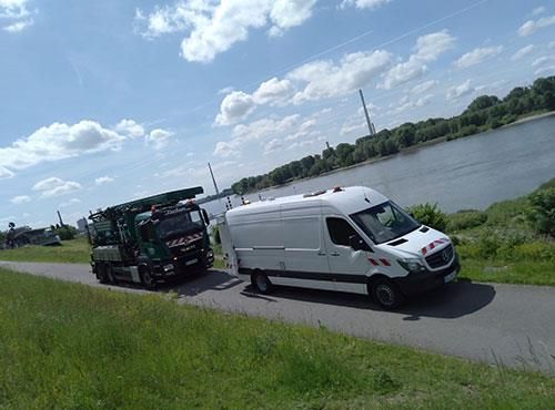 Ein weißer Lieferwagen fährt eine Straße entlang, die an einem Fluss entlangführt.