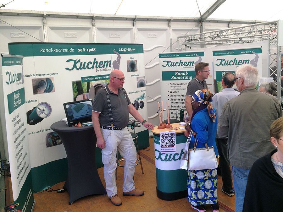 Eine Gruppe von Menschen steht um einen Stand mit der Aufschrift „Kuchem“