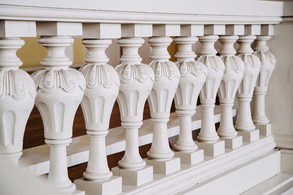 Balaustrada decorativa blanca con balaustres tallados ornamentados en un entorno interior.