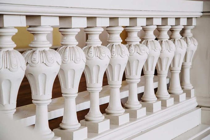 Balaustrada decorativa blanca con balaustres tallados ornamentados en un entorno interior.