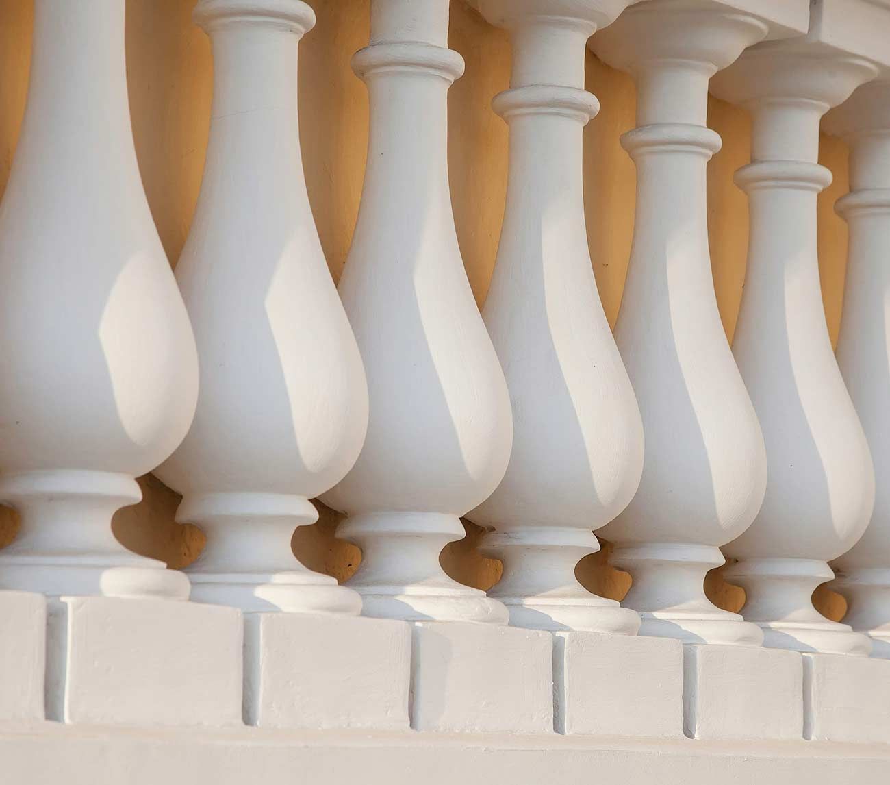 Balaustres decorativos blancos sobre una pared de color beige cálido.