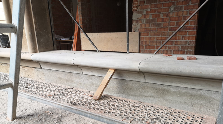 Una cornisa de piedra sostenida por madera, cerca de una pared de ladrillos y un andamio.