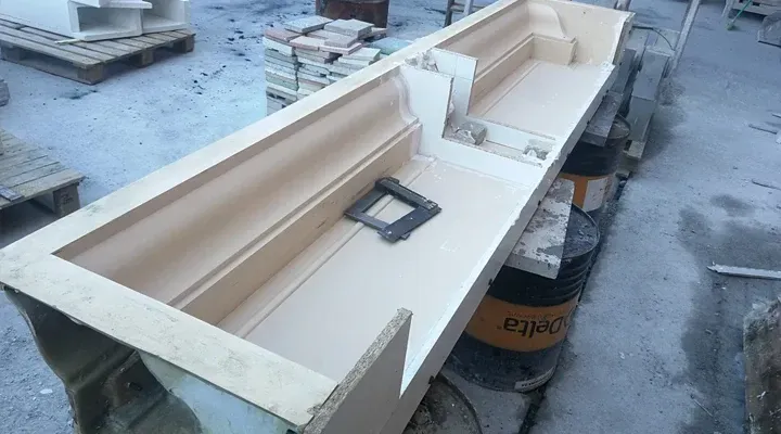 Una gran estructura rectangular de color claro, posiblemente un molde, reposa sobre soportes exteriores.