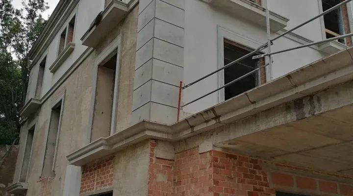 Edificio en construcción con ladrillo visto, hormigón y ventanas. Andamios visibles.