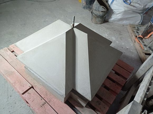 Estructura de hormigón gris y angular sobre un palé de madera, con una varilla metálica que se extiende hacia arriba.