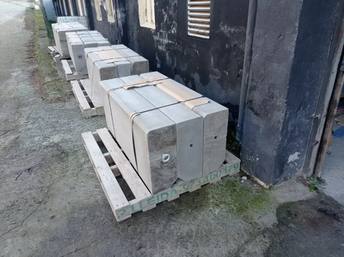 Bloques sobre paletas apiladas contra la pared oscura de un edificio sobre una superficie pavimentada.