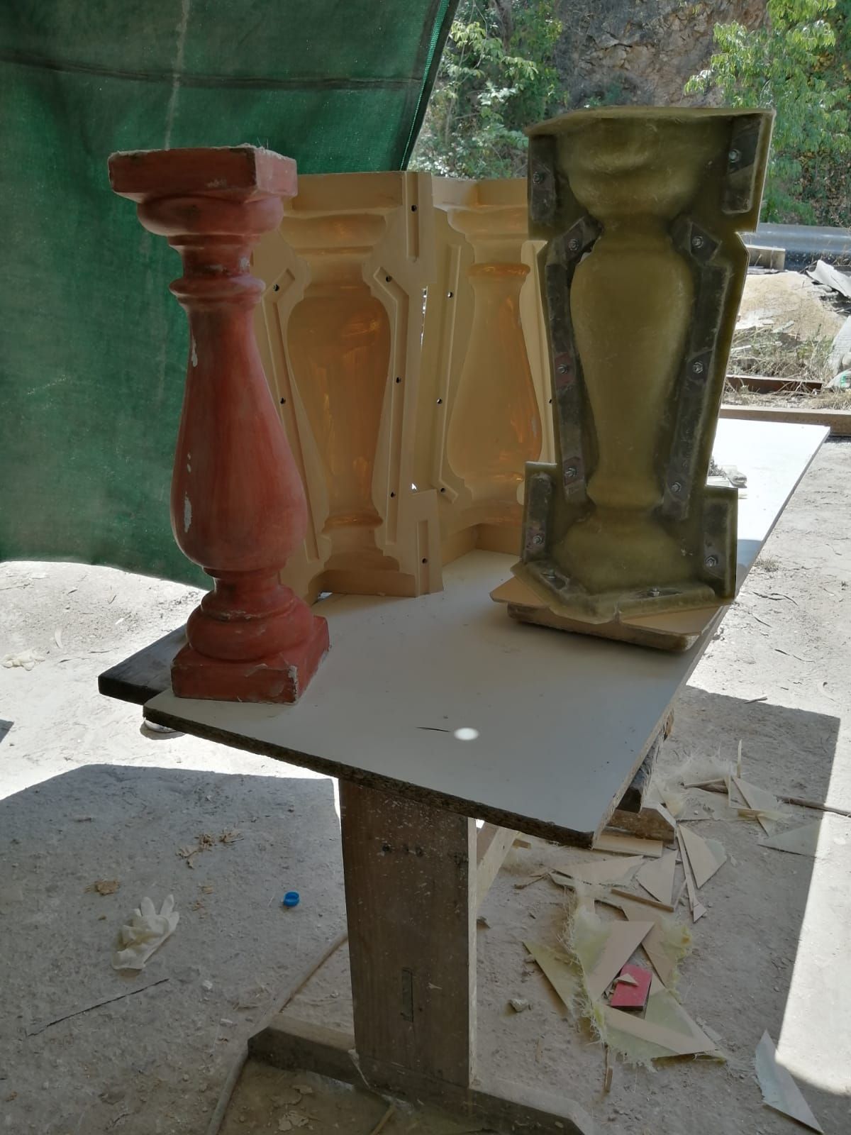 Un balaustre de hormigón rojo y varios moldes sobre una mesa, probablemente para crear más balaustres al aire libre.