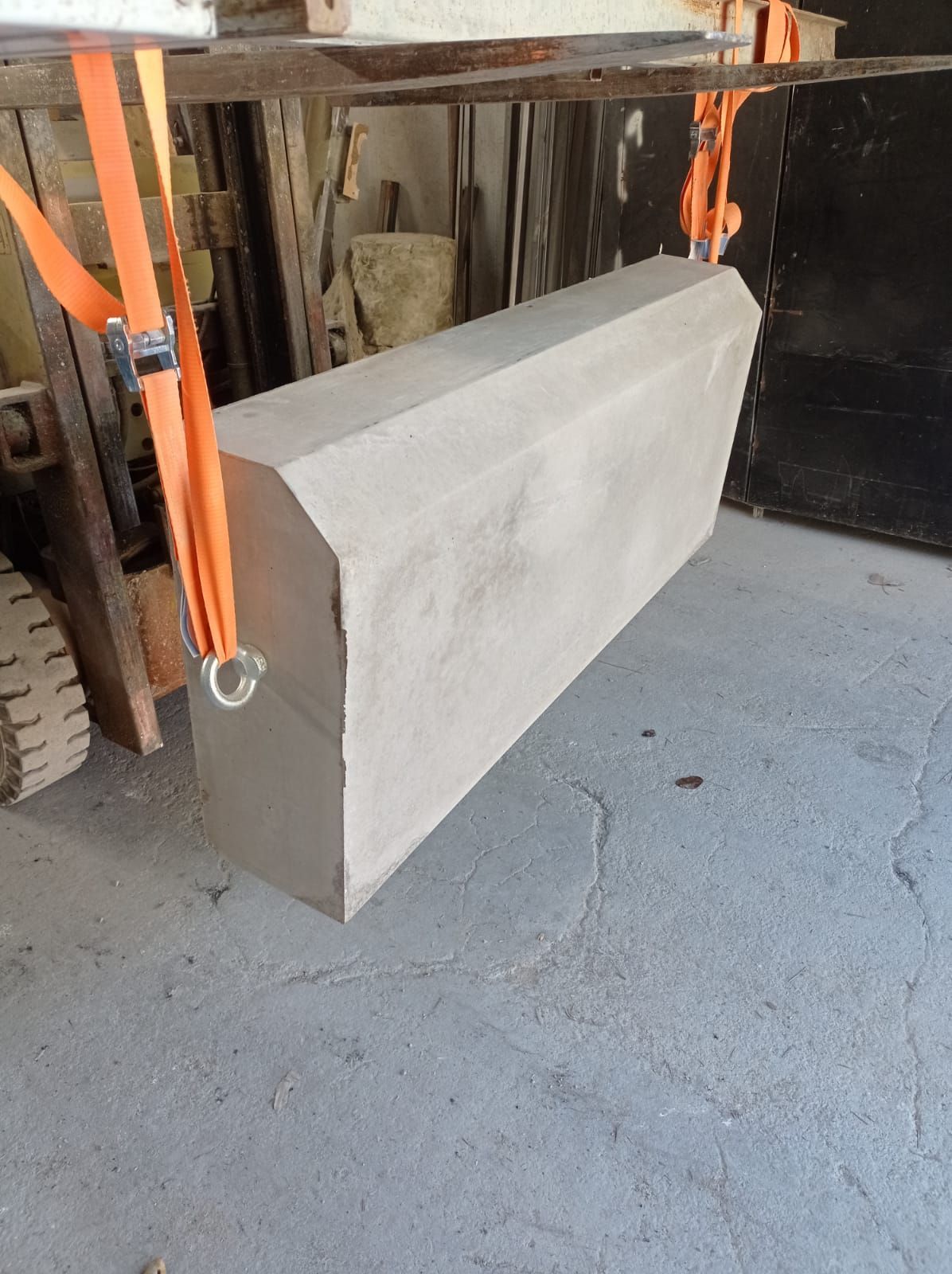Un gran bloque de piedra suspendido por correas de color naranja, probablemente para su transporte, dentro de un taller.