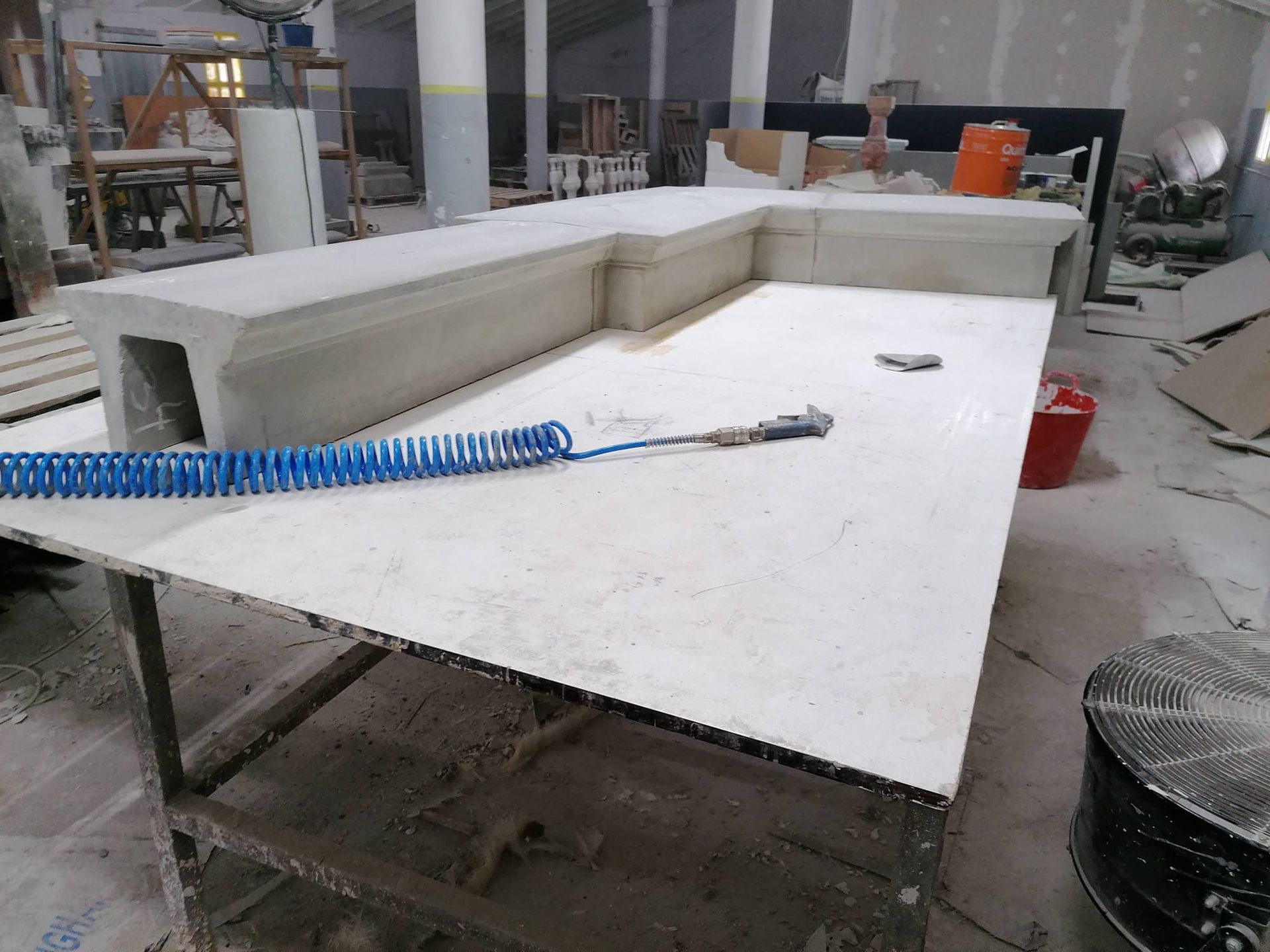 Estructura de hormigón en forma de L sobre una mesa blanca en un taller, con manguera de aire azul.
