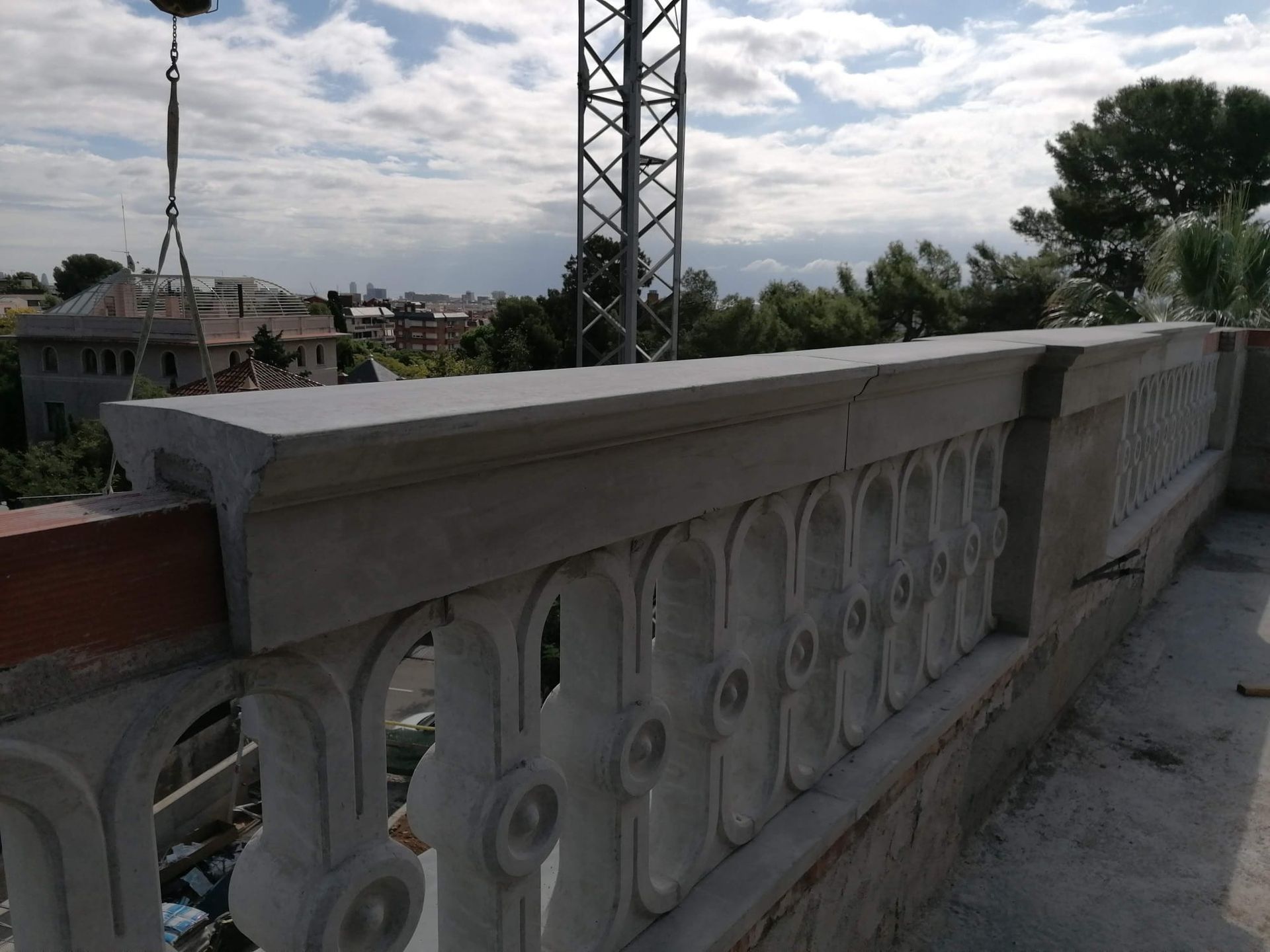 Balaustrada con tallas ornamentales, posiblemente de hormigón, sobre un tejado con vistas a una ciudad y un cielo nublado.