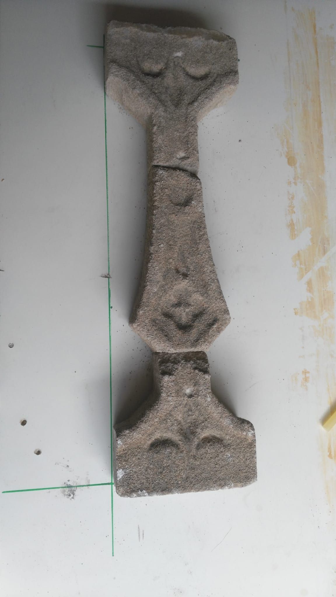 Dos fragmentos de balaustre de hormigón gris desgastado sobre una superficie blanca con una línea verde.