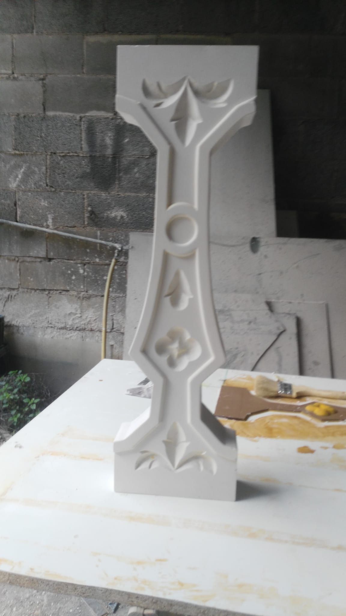 Balaustre de piedra tallada con detalles góticos, sobre una superficie blanca, contra una pared de ladrillo.