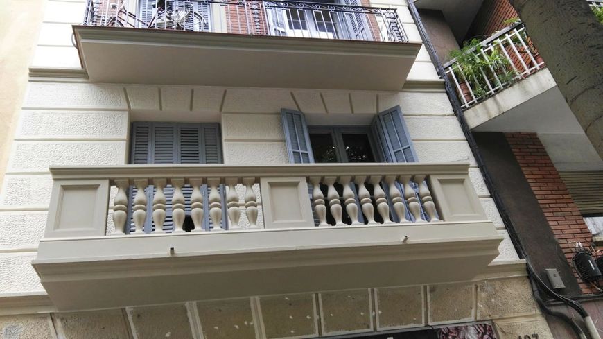 Exterior del edificio con balcones, paredes de color claro y contraventanas azules.