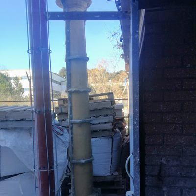 Conducto de escombros de construcción de color amarillo fijado a un edificio, sostenido por soportes metálicos.