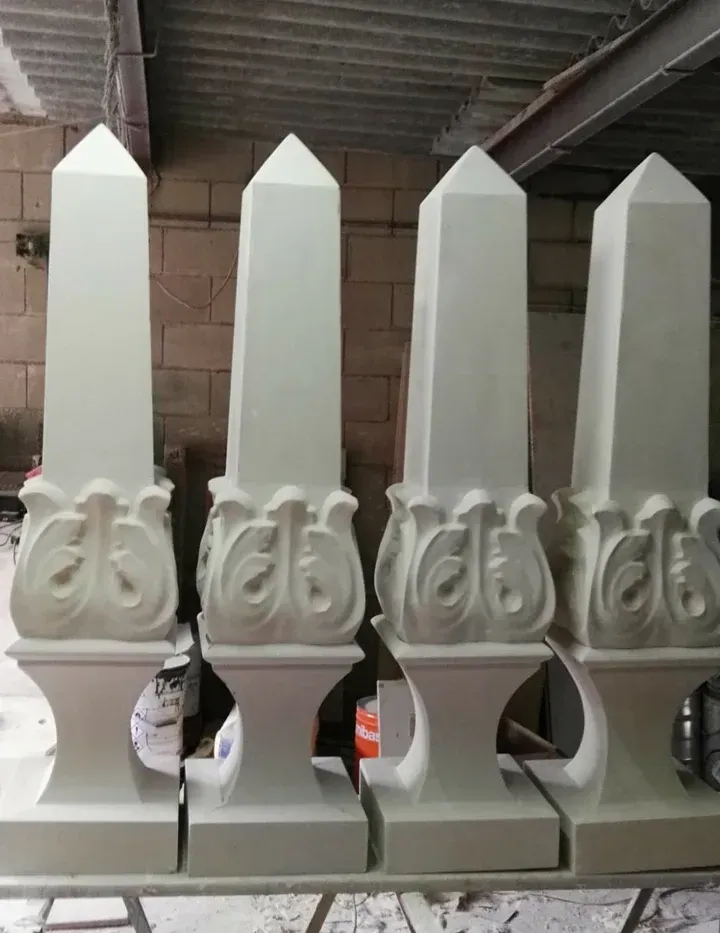 Cuatro esculturas de obelisco clásicas de color blanco con bases decorativas, alineadas en un taller.