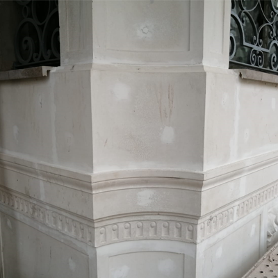 Esquina de un edificio de piedra beige claro con molduras ornamentadas y detalles decorativo