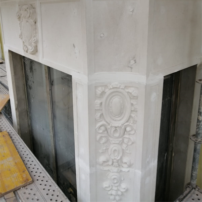 Primer plano de una chimenea de piedra blanca parcialmente construida con tallas decorativas y una abertura oscura.