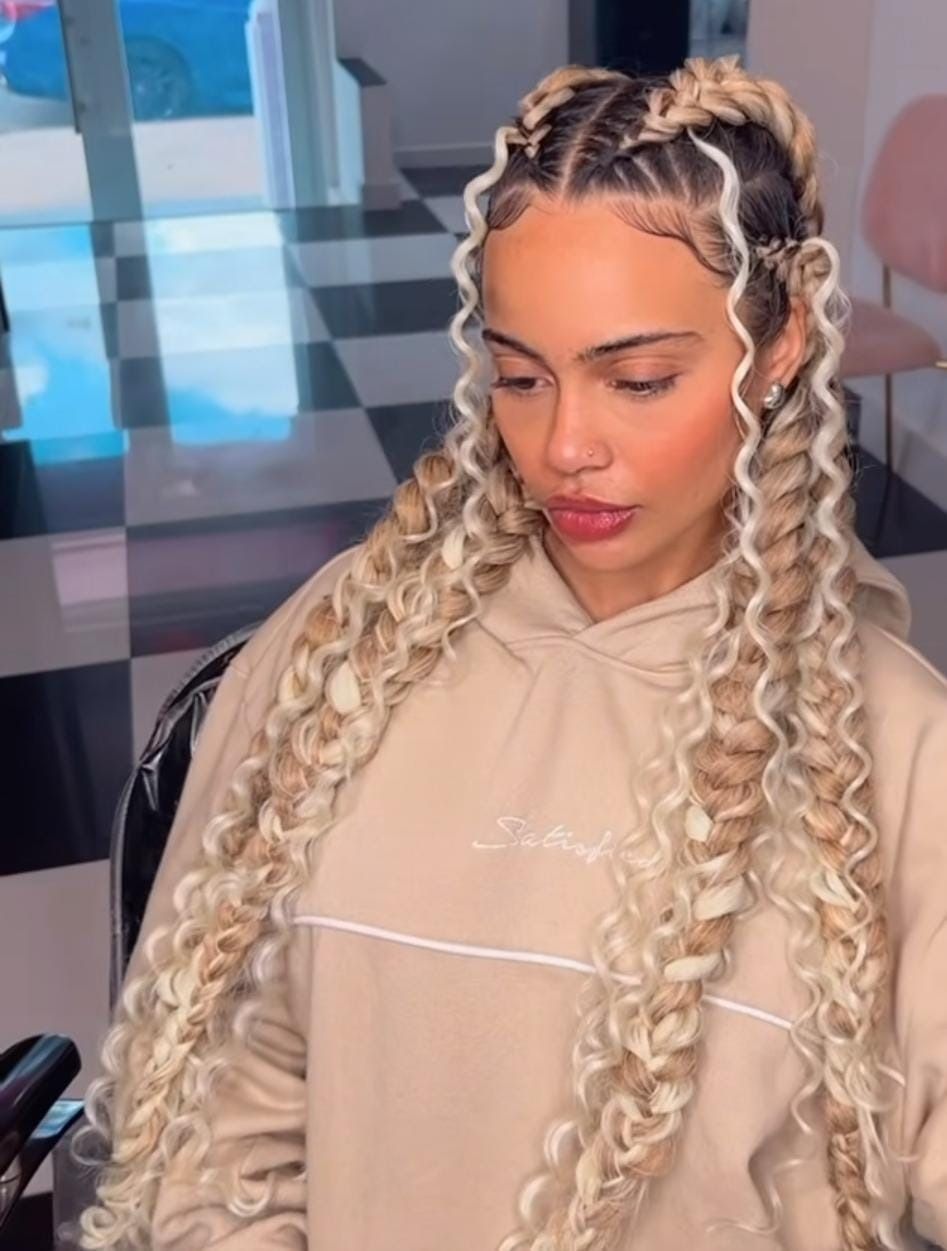 Mujer con peinado trenzado rubio, vestida con una sudadera con capucha de color canela.